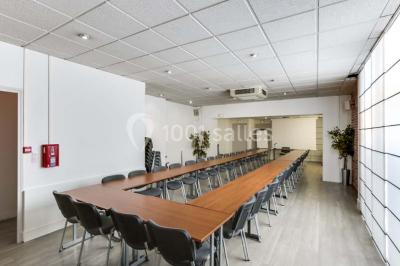 Façade d'un immeuble en pierre avec des fenêtres vitrées et un parterre de fleurs en bordure de trottoir.