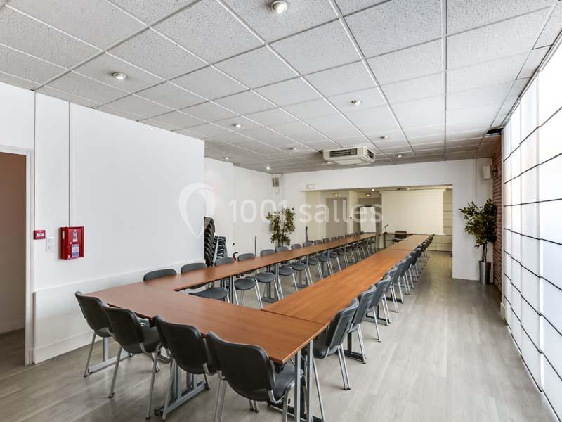 Salle de réunion lumineuse avec une grande table en U, des chaises grises et un sol en parquet clair.