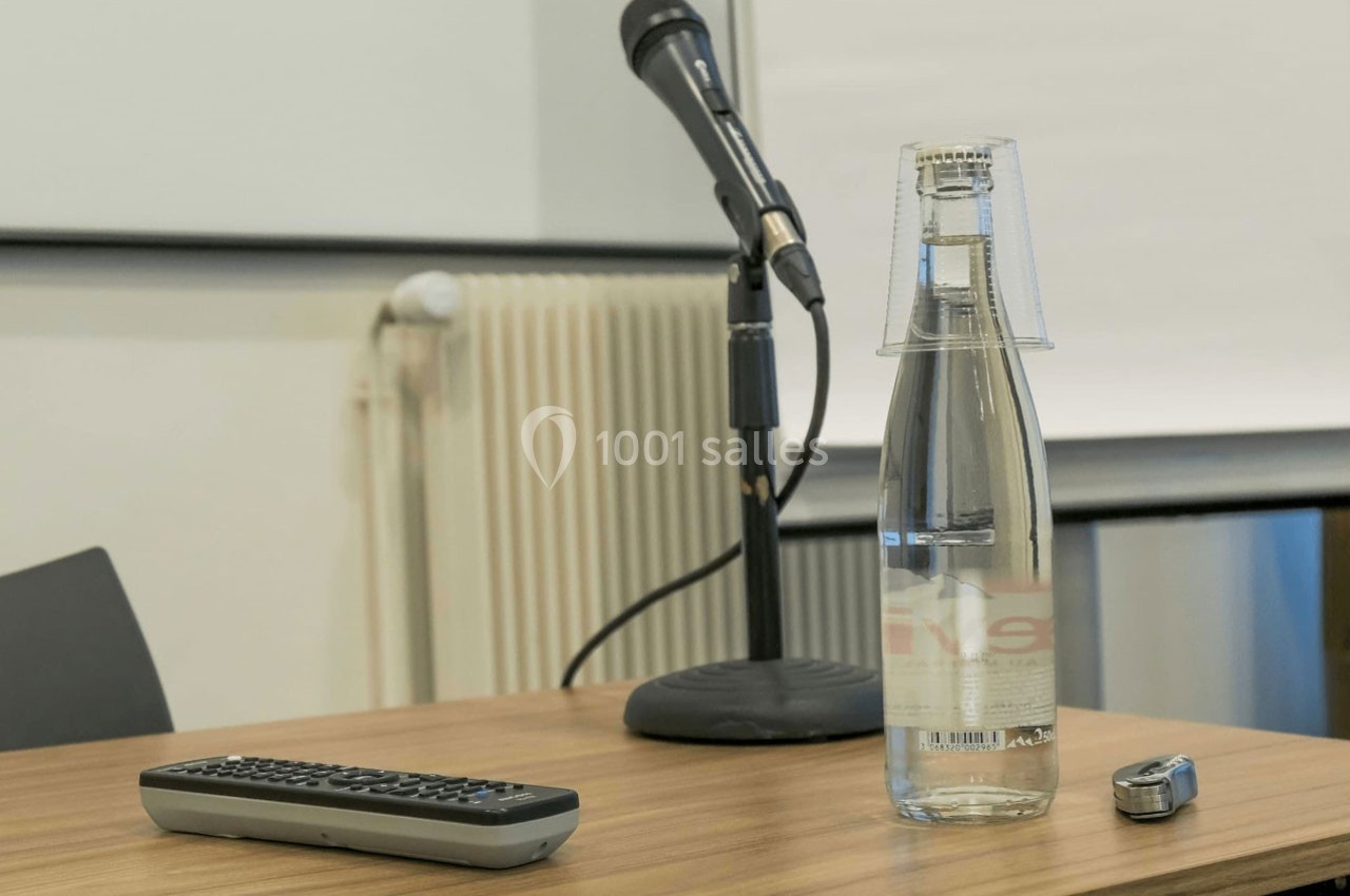 Microphone sur table en bois avec une bouteille d'eau, un verre retourné, une télécommande et un pointeur.