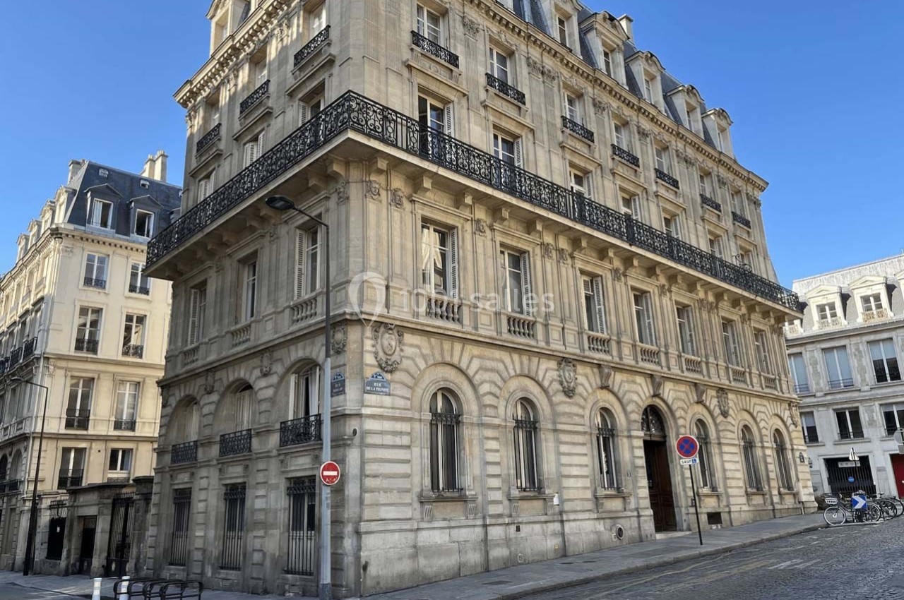 Bâtiment en pierre de style haussmannien avec balcons en fer forgé, situé à l'angle d'une rue pavée.