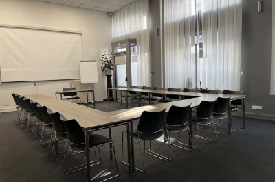 Façade d'un immeuble en pierre avec des fenêtres vitrées et un parterre de fleurs en bordure de trottoir.