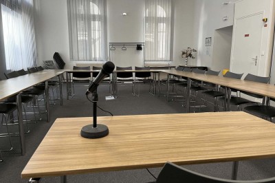 Façade d'un immeuble en pierre avec des fenêtres vitrées et un parterre de fleurs en bordure de trottoir.