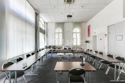 Façade d'un immeuble en pierre avec des fenêtres vitrées et un parterre de fleurs en bordure de trottoir.