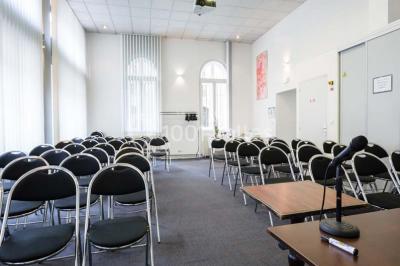 Façade d'un immeuble en pierre avec des fenêtres vitrées et un parterre de fleurs en bordure de trottoir.