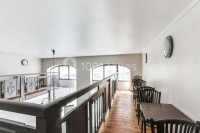 Façade d'un immeuble en pierre avec des fenêtres vitrées et un parterre de fleurs en bordure de trottoir.