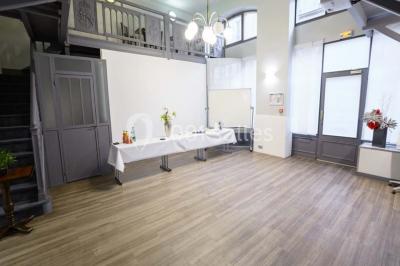 Façade d'un immeuble en pierre avec des fenêtres vitrées et un parterre de fleurs en bordure de trottoir.