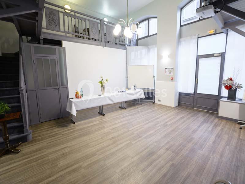 Salle lumineuse avec parquet, tables dressées pour un buffet, escalier et mezzanine en arrière-plan.