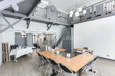 Façade d'un immeuble en pierre avec des fenêtres vitrées et un parterre de fleurs en bordure de trottoir.