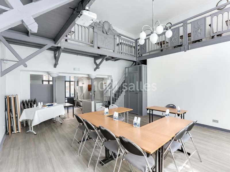 Salle lumineuse avec tables en bois, chaises pliantes, mezzanine, et buffet installé sur le côté.
