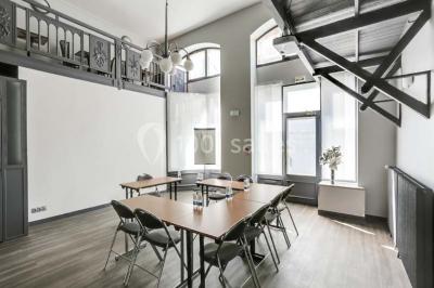 Façade d'un immeuble en pierre avec des fenêtres vitrées et un parterre de fleurs en bordure de trottoir.