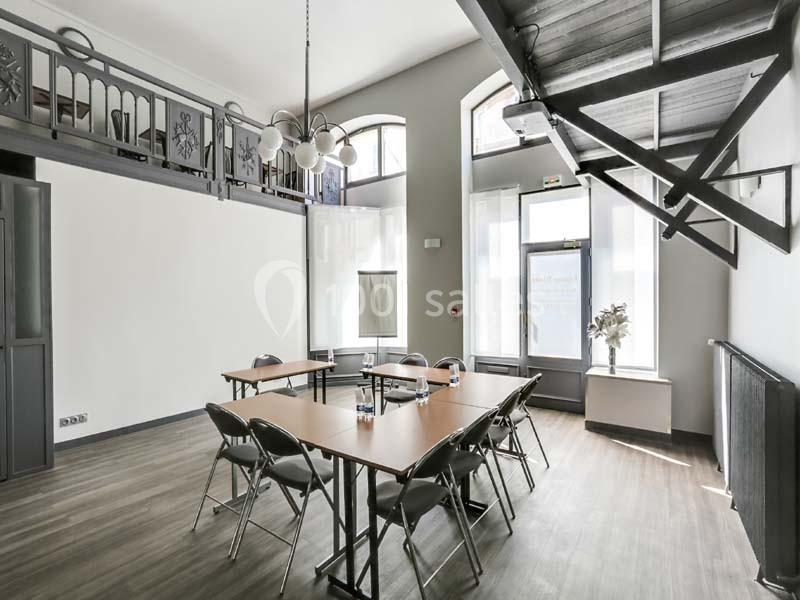 Salle lumineuse avec tables et chaises disposées pour une réunion, mezzanine et grandes fenêtres en arrière-plan.