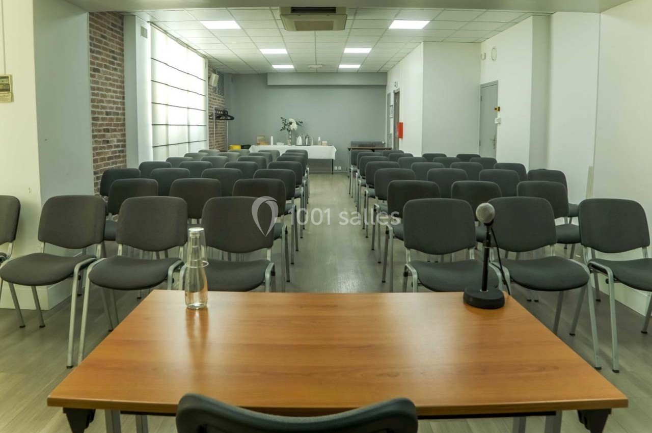 Salle de conférence vide avec des rangées de chaises grises, une table en bois avec un micro et une bouteille d'eau au…