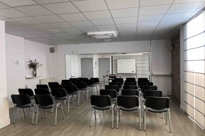 Façade d'un immeuble en pierre avec des fenêtres vitrées et un parterre de fleurs en bordure de trottoir.