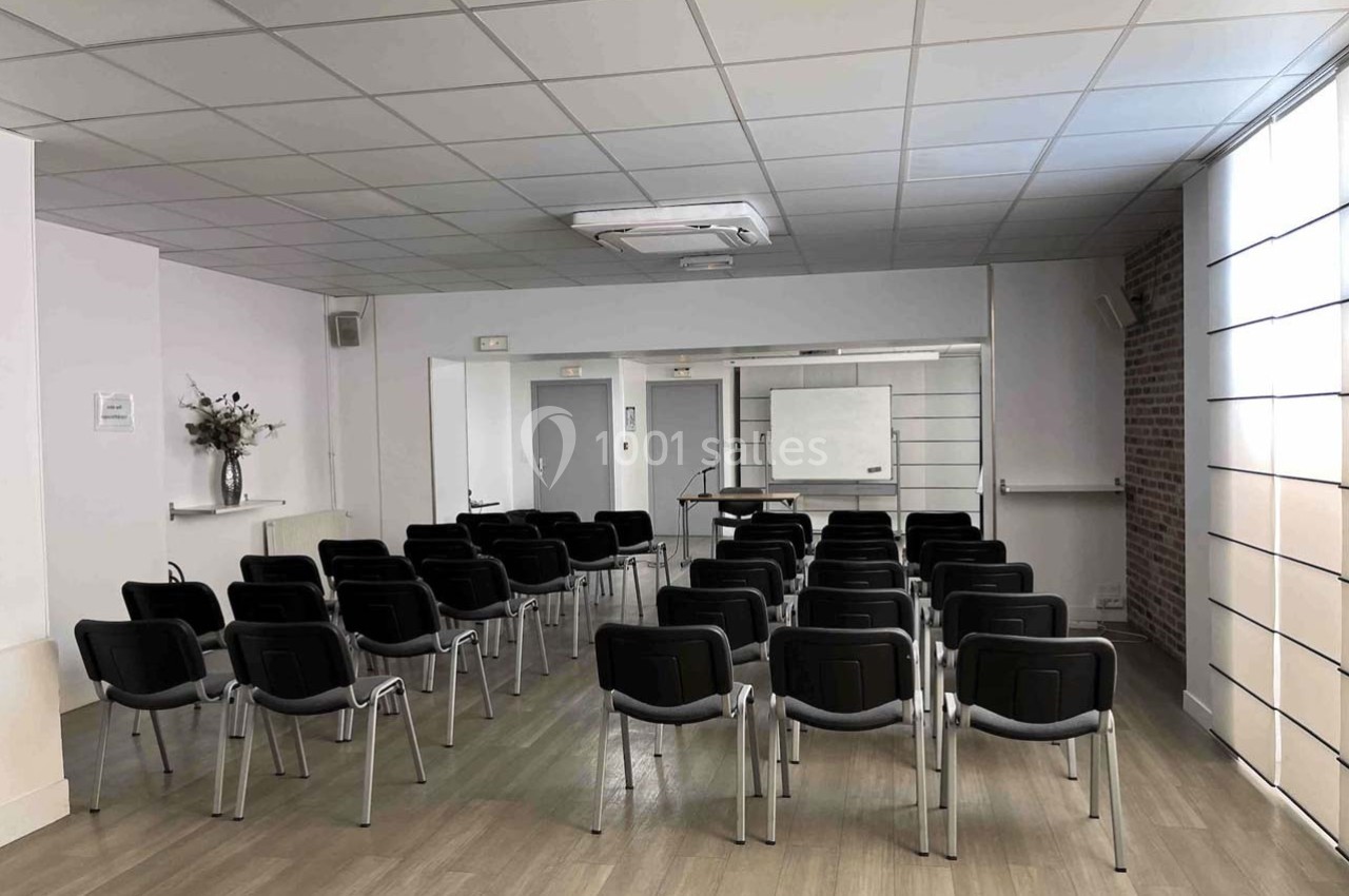 Salle de réunion lumineuse avec des rangées de chaises noires, un tableau blanc et un pupitre à l'avant.