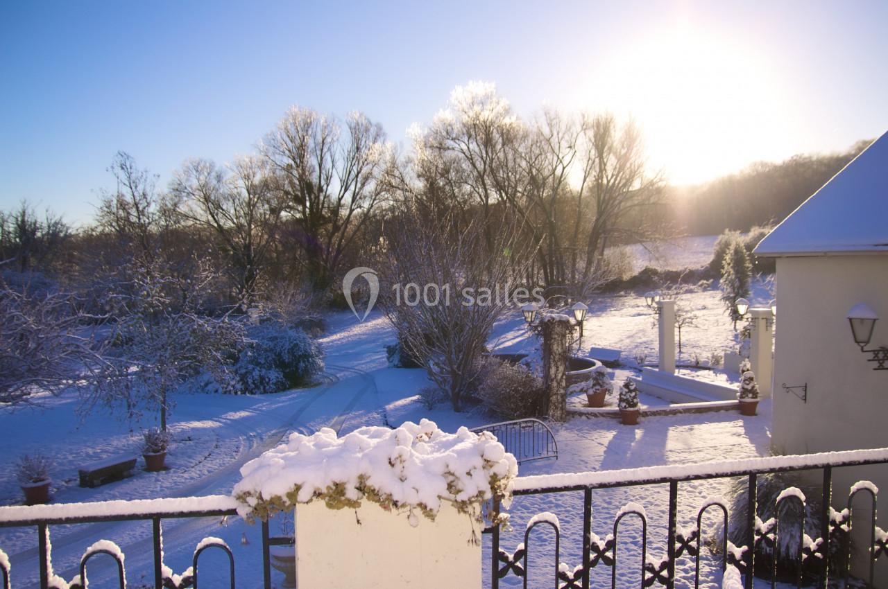 Paysage enneigé au lever du soleil, avec un jardin, des arbres givrés et une maison partiellement visible.