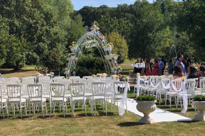 Arrangements floraux sur des supports en bois disposés sur une table recouverte d'une nappe blanche devant un mur en pierre.