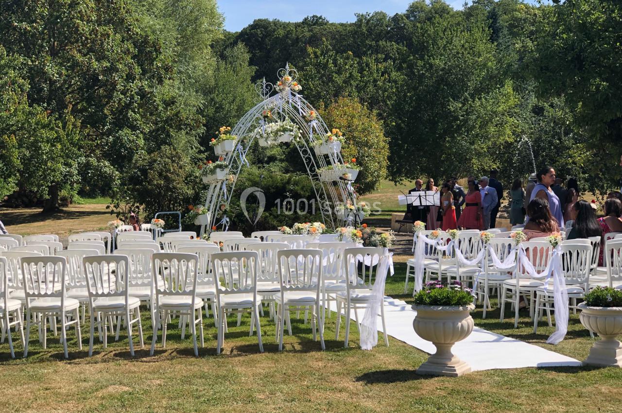 Chaises blanches alignées devant une arche décorée de fleurs dans un jardin pour une cérémonie en plein air.