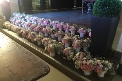 Arrangements floraux sur des supports en bois disposés sur une table recouverte d'une nappe blanche devant un mur en pierre.