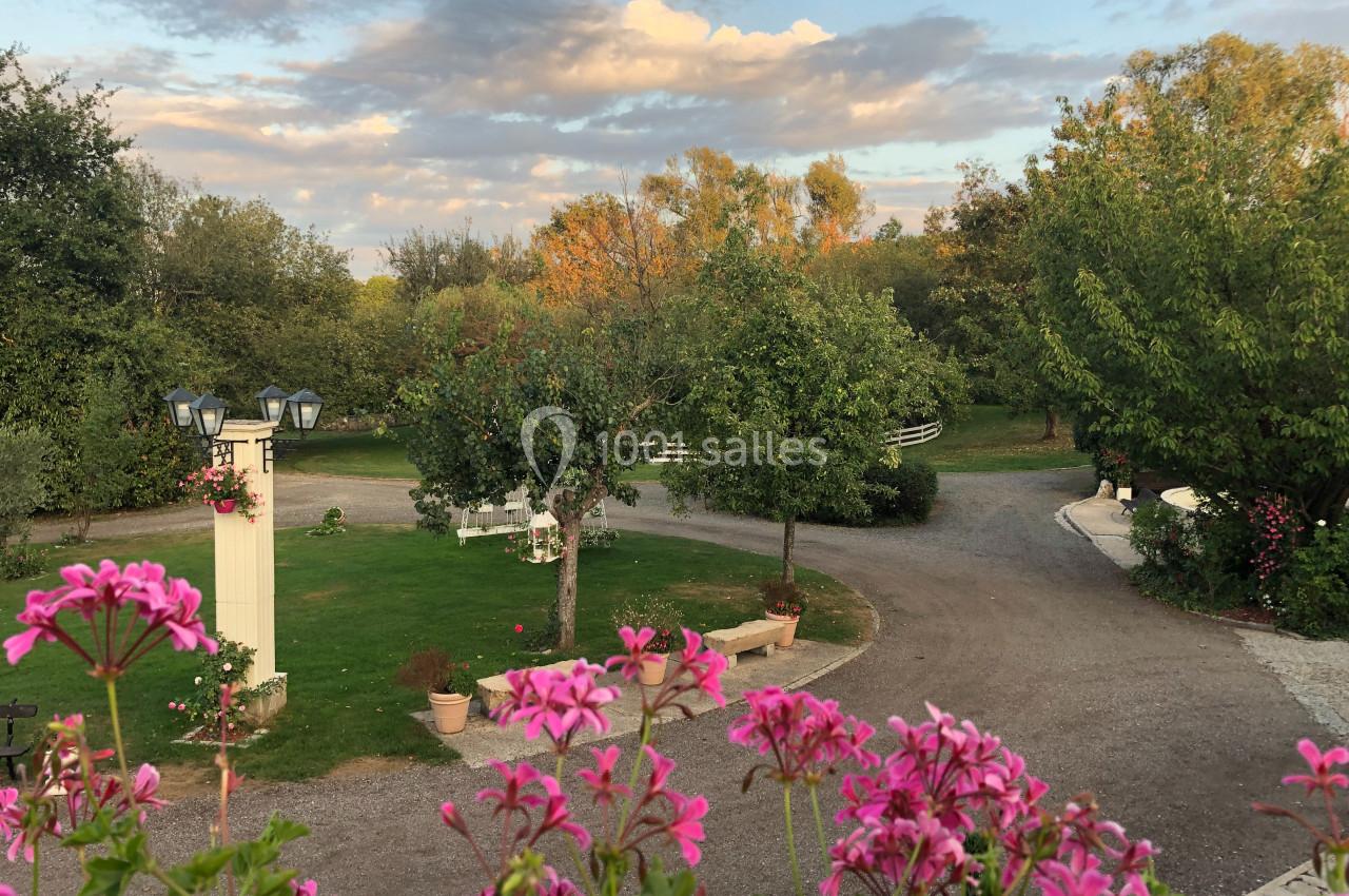 Allée sinueuse bordée d'arbres et de fleurs roses dans un jardin sous un ciel partiellement nuageux.