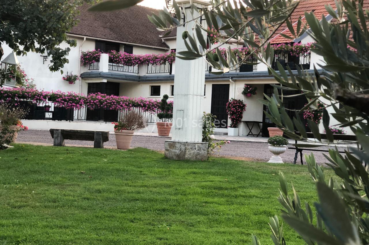 Cour verdoyante avec bancs, colonne décorative et bâtiment fleuri en arrière-plan.