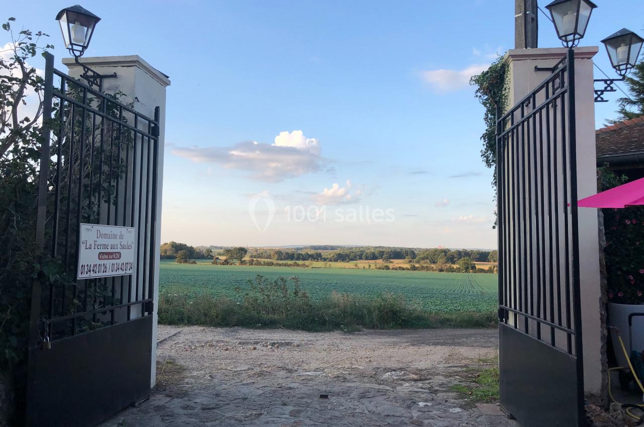 Vue sur un champ verdoyant à travers un portail ouvert en fer forgé, sous un ciel dégagé en fin de journée.