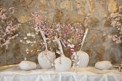 Arrangements floraux sur des supports en bois disposés sur une table recouverte d'une nappe blanche devant un mur en pierre.