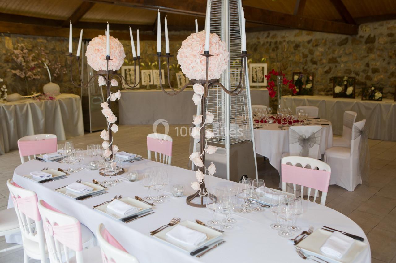 Salle de réception décorée avec des tables dressées, des chaises ornées de rubans roses et des centres de table fleuris.