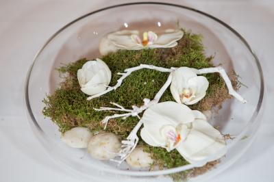 Arrangements floraux sur des supports en bois disposés sur une table recouverte d'une nappe blanche devant un mur en pierre.