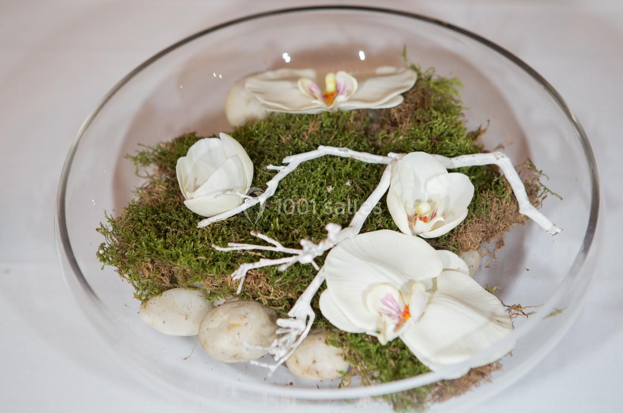 Composition florale avec des orchidées blanches, de la mousse, des branches blanches et des galets dans un récipient en…