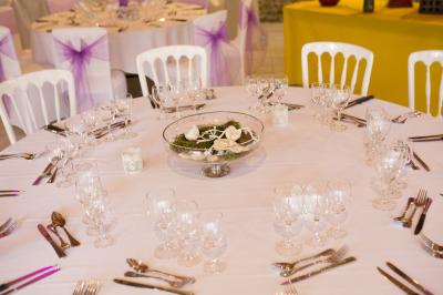 Arrangements floraux sur des supports en bois disposés sur une table recouverte d'une nappe blanche devant un mur en pierre.