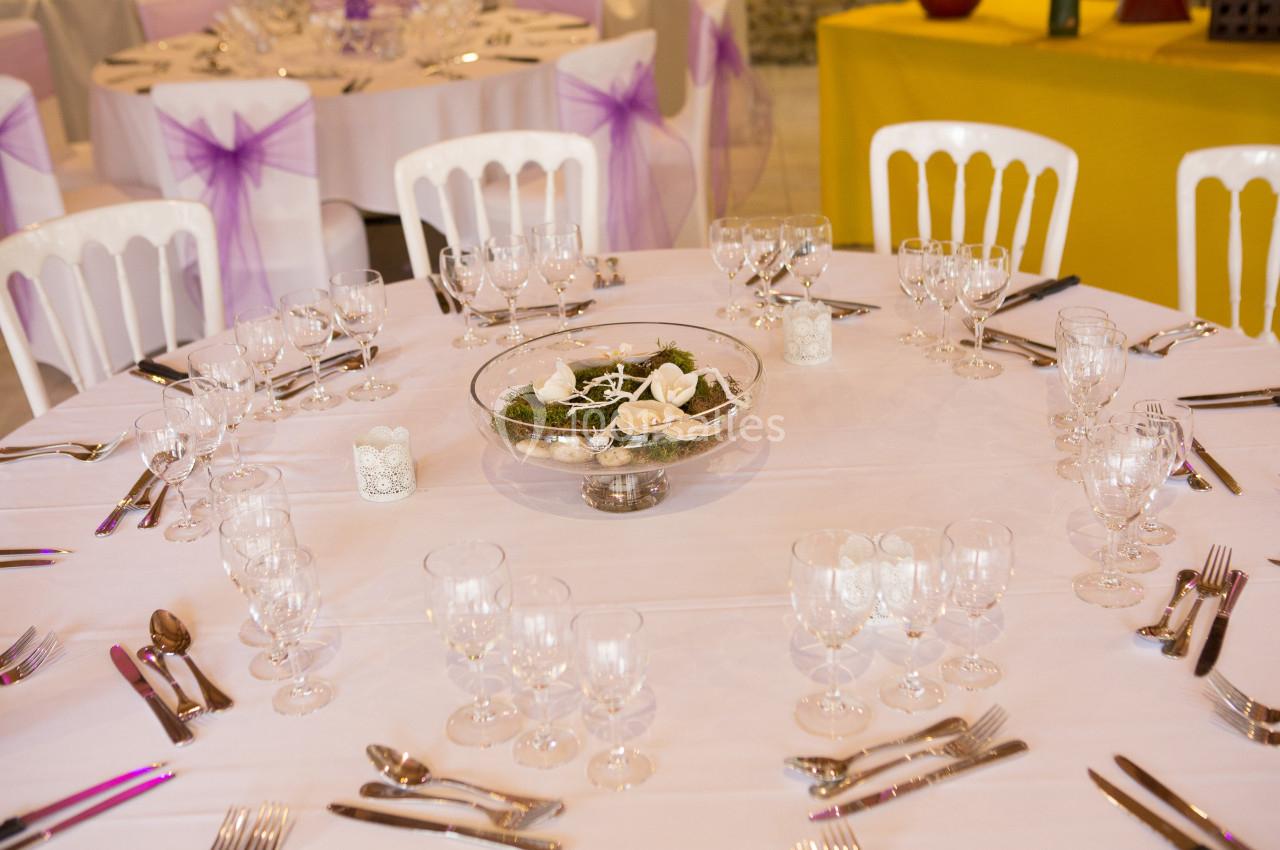 Table ronde dressée pour un événement, avec nappes blanches, verres, couverts et centre de table décoratif.