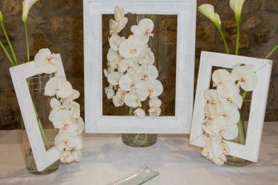 Arrangements floraux sur des supports en bois disposés sur une table recouverte d'une nappe blanche devant un mur en pierre.