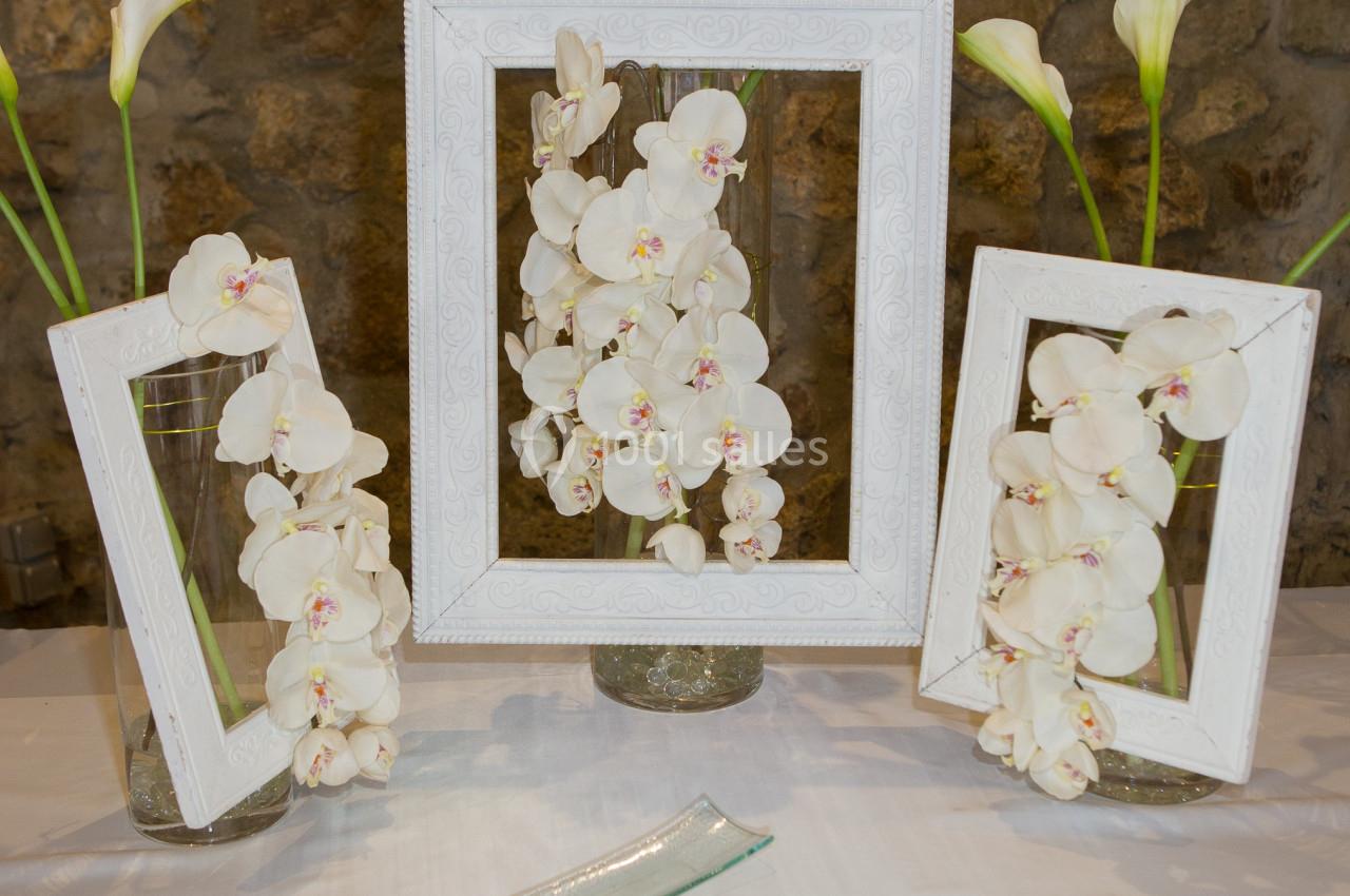 Arrangement floral avec des orchidées blanches et des callas dans des vases, encadrés par des cadres blancs, sur une table.