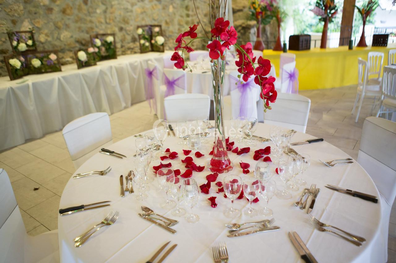 Table ronde décorée avec une nappe blanche, des pétales rouges, un vase central fleuri et des couverts disposés.