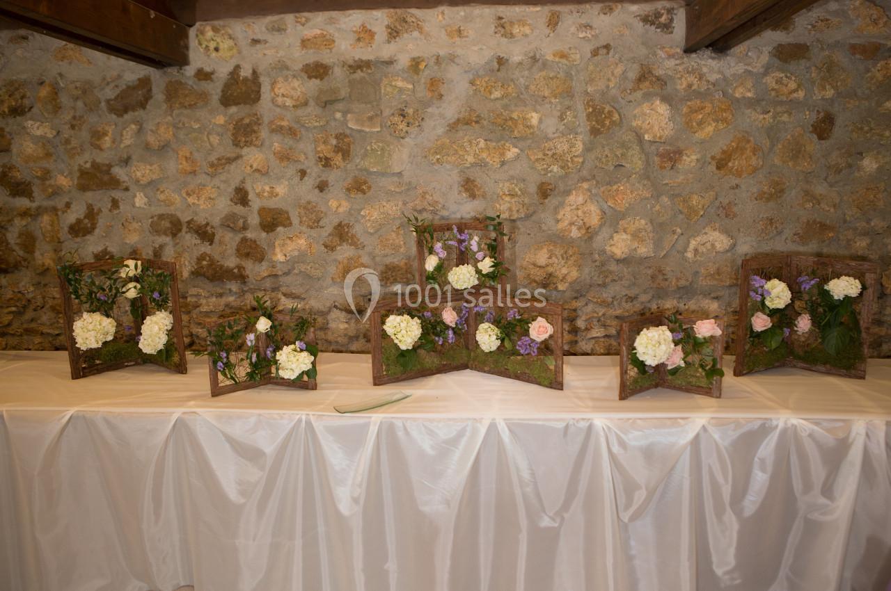 Arrangements floraux sur des supports en bois disposés sur une table recouverte d'une nappe blanche devant un mur en pierre.