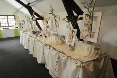 Arrangements floraux sur des supports en bois disposés sur une table recouverte d'une nappe blanche devant un mur en pierre.