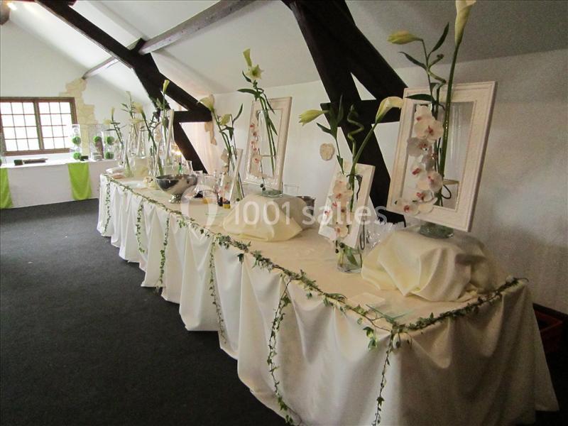 Table décorée avec nappes blanches, vases contenant des fleurs blanches et guirlandes végétales dans une salle lumineuse.
