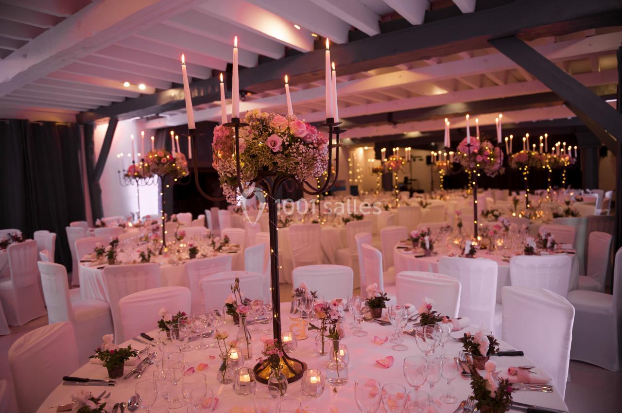 Salle de réception décorée avec des chandeliers, des fleurs roses et des tables dressées pour un événement.