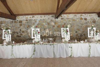 Arrangements floraux sur des supports en bois disposés sur une table recouverte d'une nappe blanche devant un mur en pierre.
