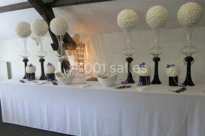 Arrangements floraux sur des supports en bois disposés sur une table recouverte d'une nappe blanche devant un mur en pierre.