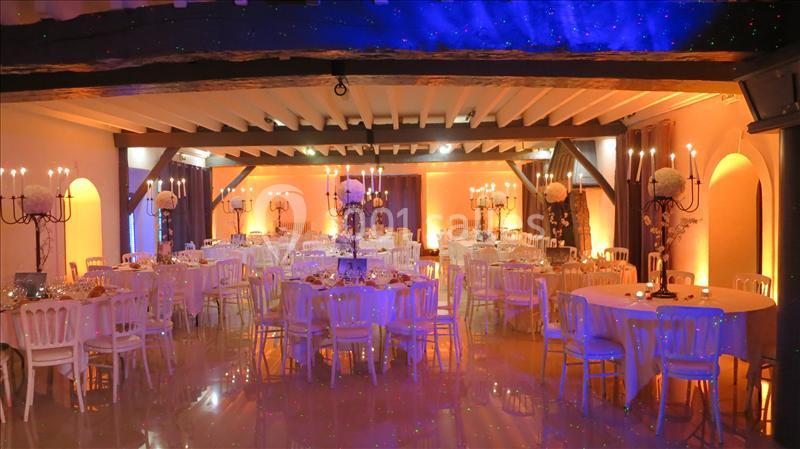 Salle de réception décorée avec des tables rondes, des chandeliers et un éclairage chaleureux.