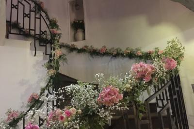 Arrangements floraux sur des supports en bois disposés sur une table recouverte d'une nappe blanche devant un mur en pierre.