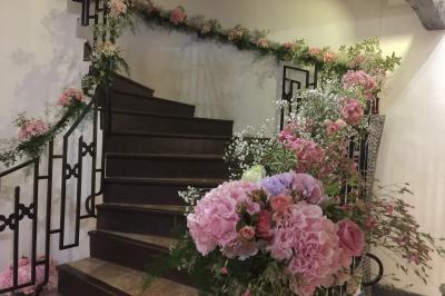 Arrangements floraux sur des supports en bois disposés sur une table recouverte d'une nappe blanche devant un mur en pierre.