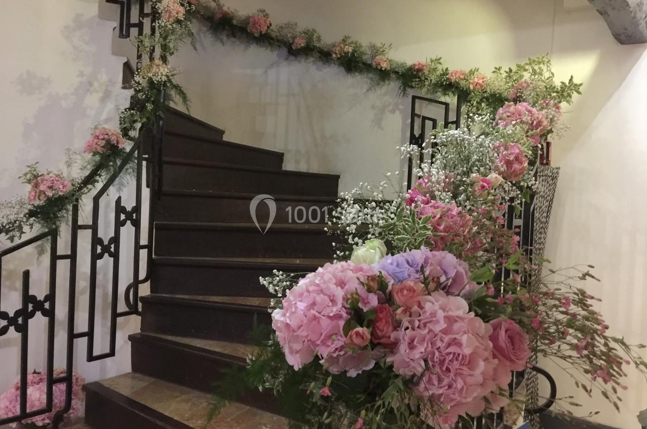 Escalier décoré de guirlandes de fleurs roses et blanches, avec des bouquets disposés au premier plan.