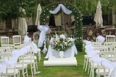 Arrangements floraux sur des supports en bois disposés sur une table recouverte d'une nappe blanche devant un mur en pierre.