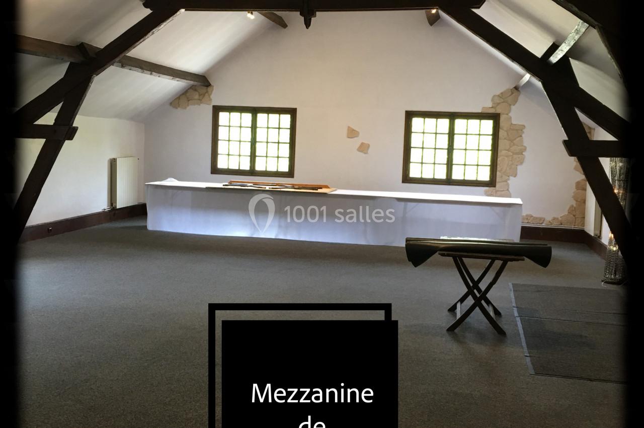 Salle de réception avec poutres apparentes, grandes fenêtres et une table recouverte d'une nappe blanche.