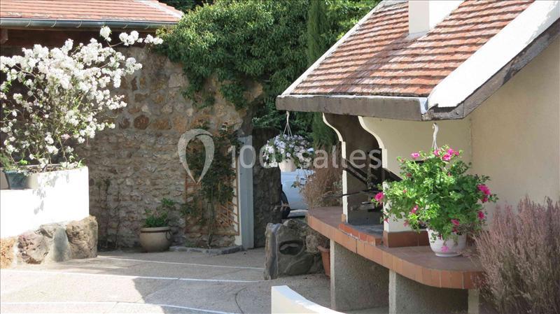 Cour extérieure avec un four à bois, des pots de fleurs colorées et des murs en pierre entourés de végétation.