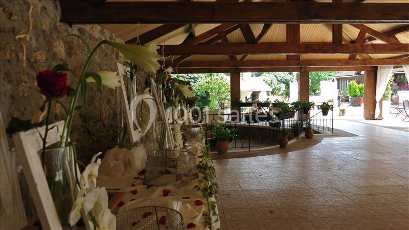 Salle de réception avec décoration florale, murs en pierre, poutres en bois et vue sur un espace extérieur verdoyant.