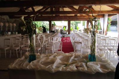 Arrangements floraux sur des supports en bois disposés sur une table recouverte d'une nappe blanche devant un mur en pierre.