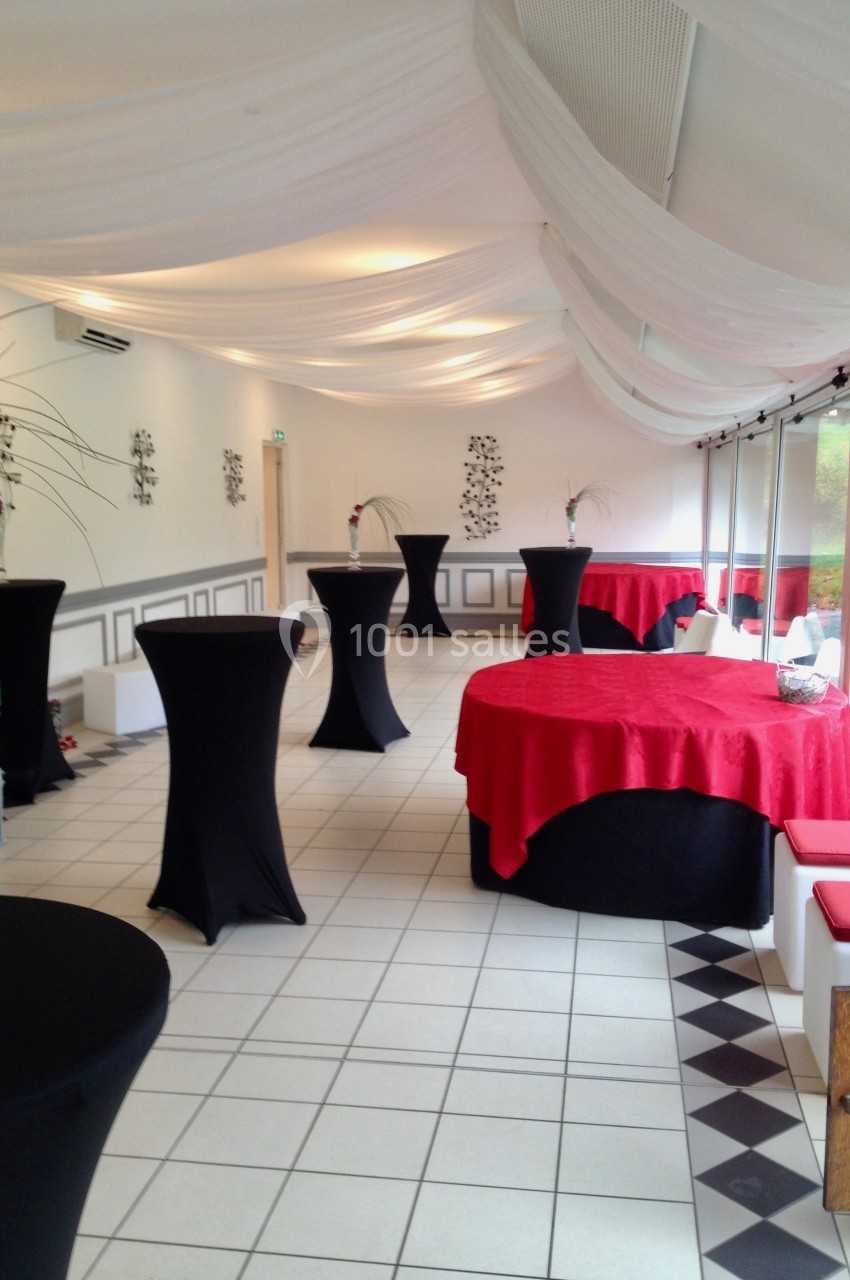 Salle de réception lumineuse avec tables hautes noires et tables rondes recouvertes de nappes rouges.